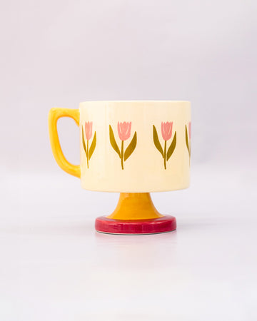 side view of top view of cream 10 oz ceramic mug with yellow handle, pink pedestal base and pink tulip print