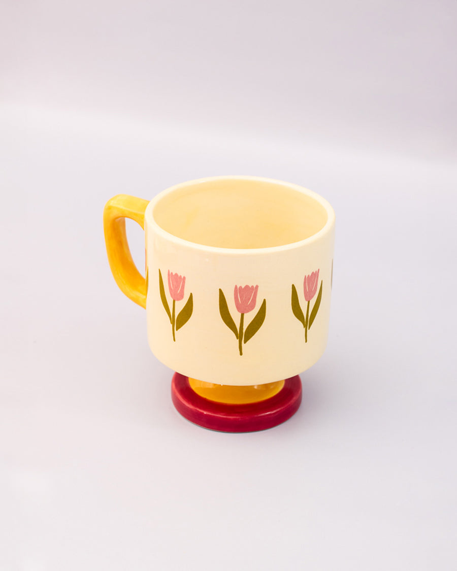 top view of cream 10 oz ceramic mug with yellow handle, pink pedestal base and pink tulip print