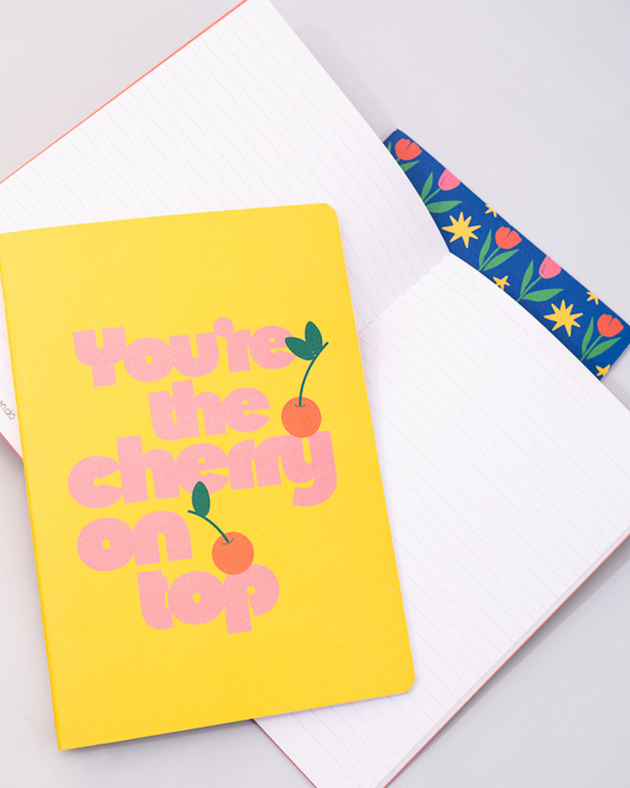 set of three notebook set: dark blue with tulip print, yellow with 'you're the cherry on top' typography, and pink mid century tulips with one opened to show lined paper