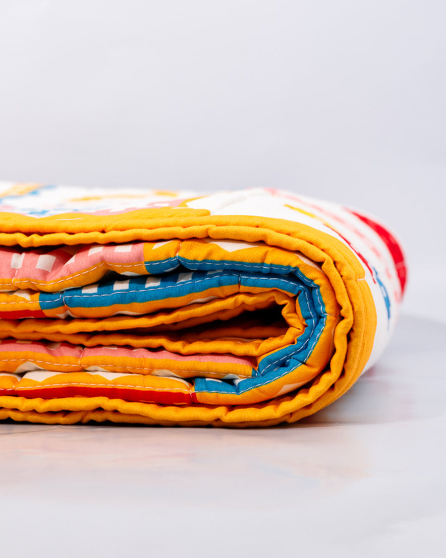 side view of colorful patchwork quilted blanket with heart, shamrocks, pretzels, smiley faces, cakes, and bows to show thickness