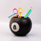 side view of black magic 8 ball shaped vase with pencils and desk accessories inside