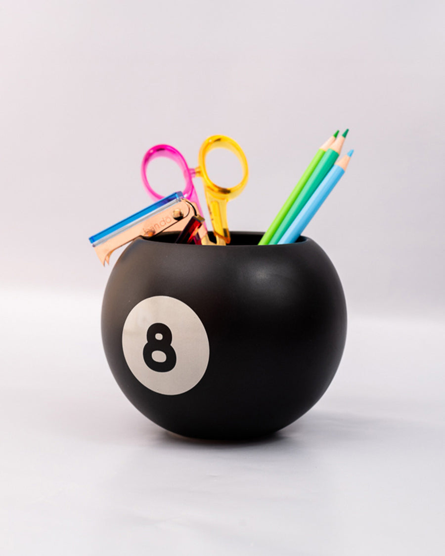 side view of black magic 8 ball shaped vase with pencils and desk accessories inside