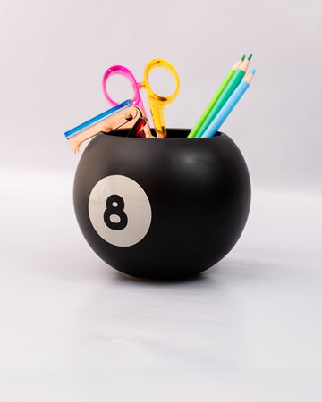 side view of black magic 8 ball shaped vase with pencils and desk accessories inside