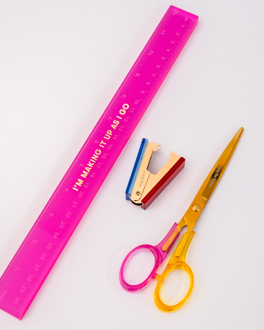 side view of desk set with pink acrylic ruler with gold 'i'm making it up as i go', colorful acrylic staple remover and scissors