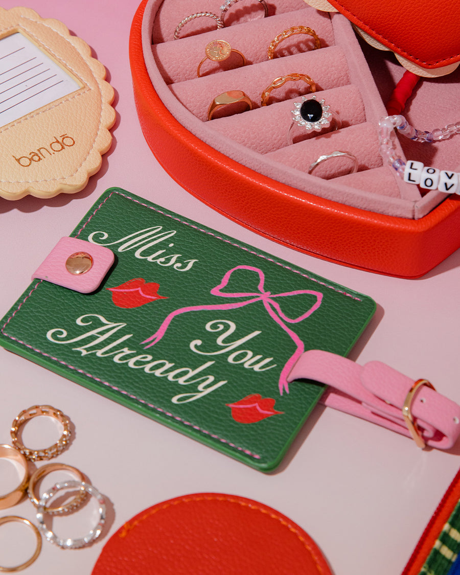 green luggage tag with pink strap and trim with 'miss you already' in cursive surrounded by cute items