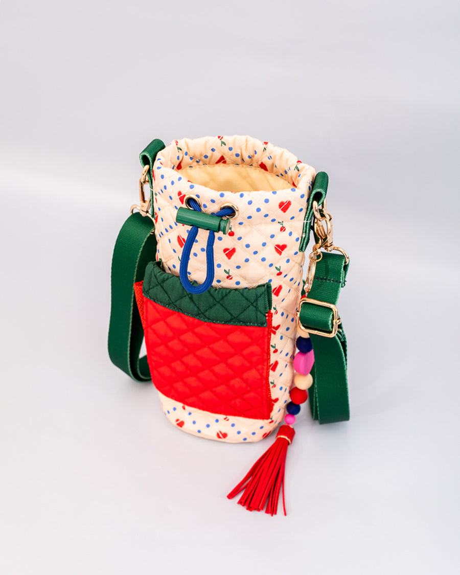 side view of cream quilted water bottle sling with red and green front pouch, green adjustable strap and colorful beaded tassel keychain