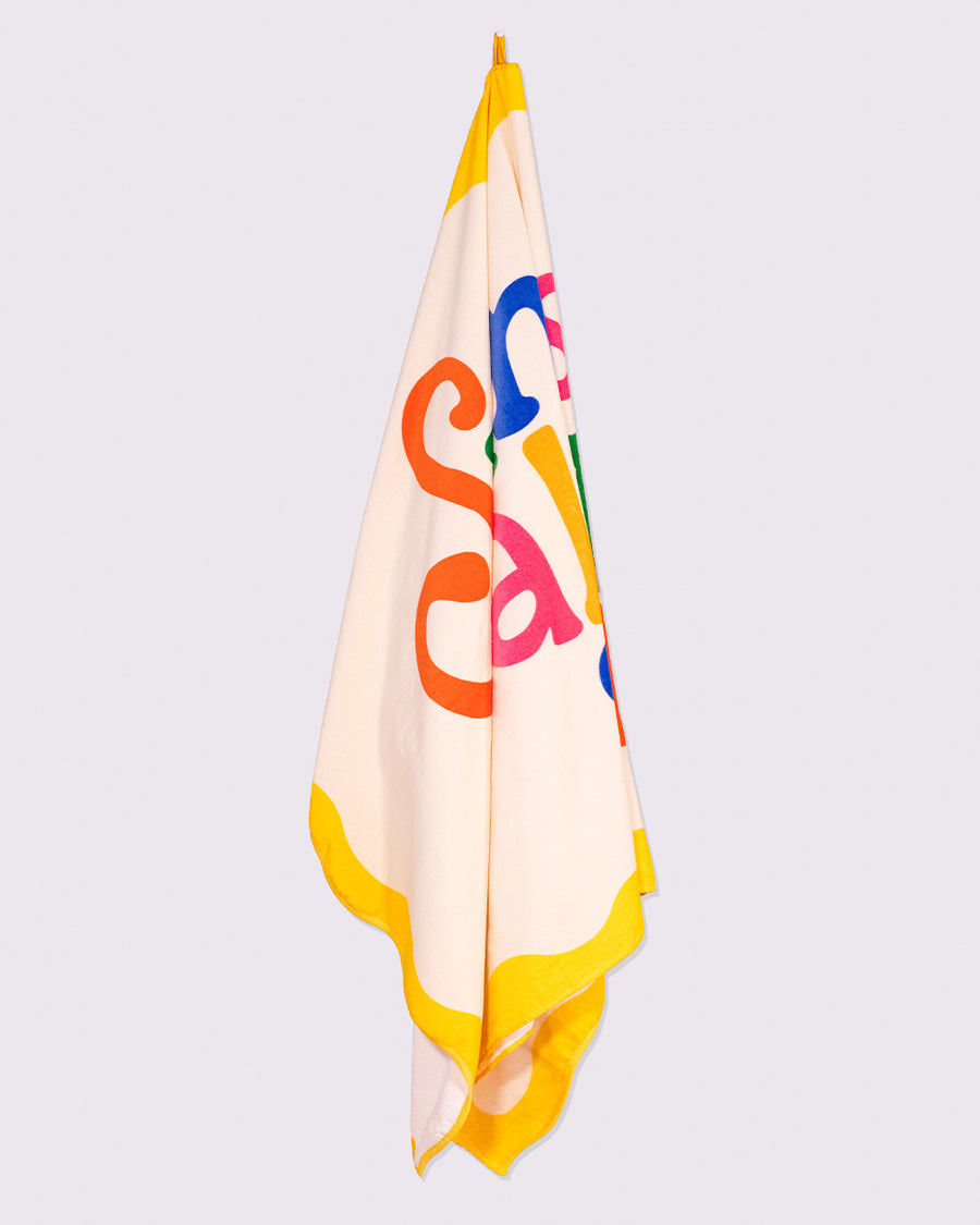 cream oversized towel with colorful 'sunshine all the time' typography and yellow scalloped trim hanging from a hook