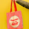 model holding reverse side of tote bag that says 'tomatoes are the best' with yellow and red vertical stripes and red handle