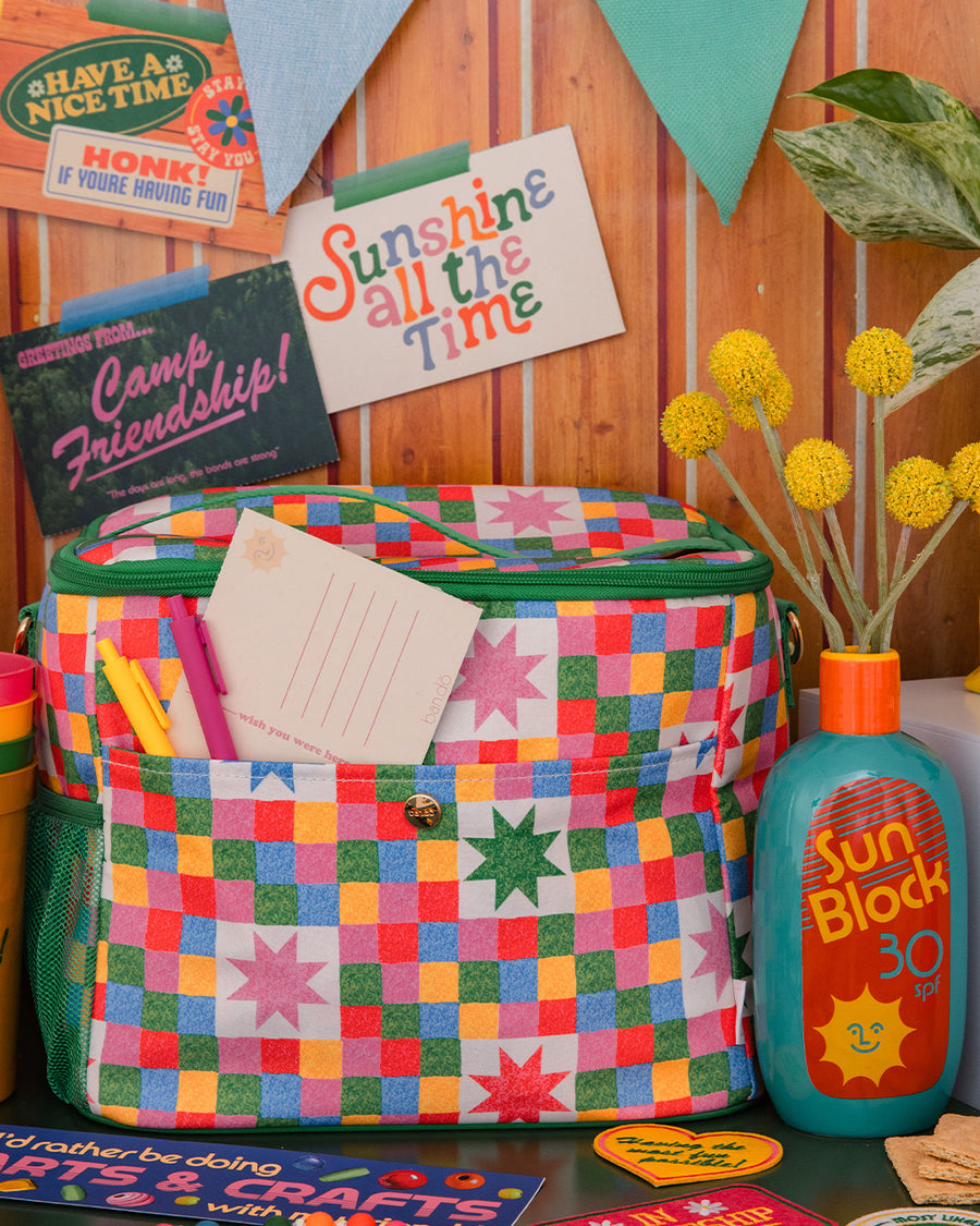 colorful 'quilted' star lunch bag with green trim and strap and front pocket and sunblock vase next to it