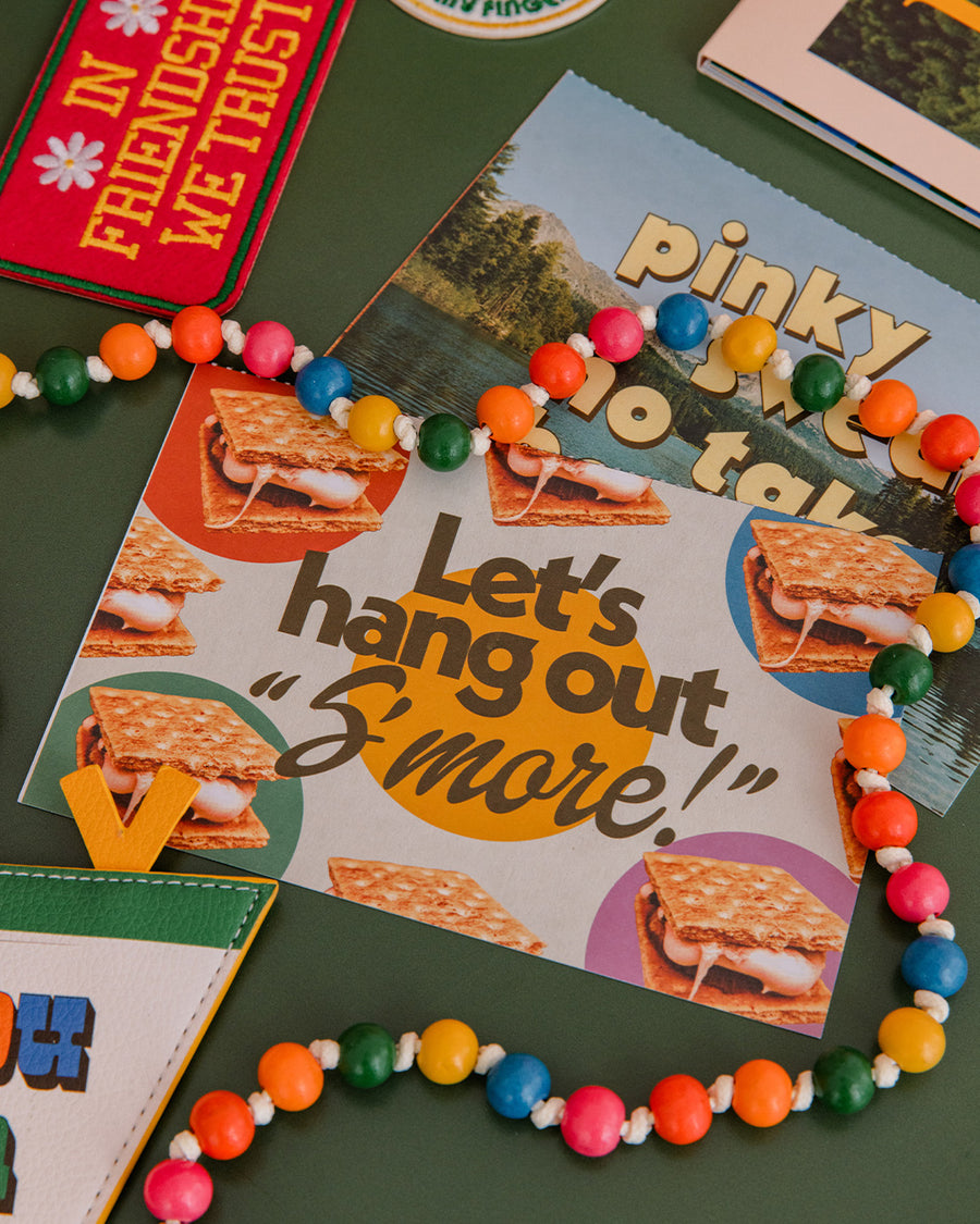 colorful beaded crossbody phone lanyard with gold carabiners laying on a table with postcards scattered