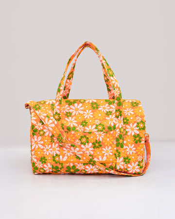 orange quilted duffel bag with handles and adjustable strap and has an all over yellow, white, and green retro floral print