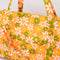 up close of orange quilted duffel bag with handles and adjustable strap and has an all over yellow, white, and green retro floral print