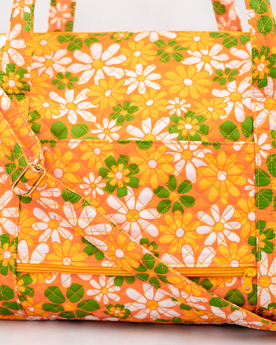 up close of suitcase sleeve and zipper pouch of orange quilted duffel bag with handles and adjustable strap and has an all over yellow, white, and green retro floral print