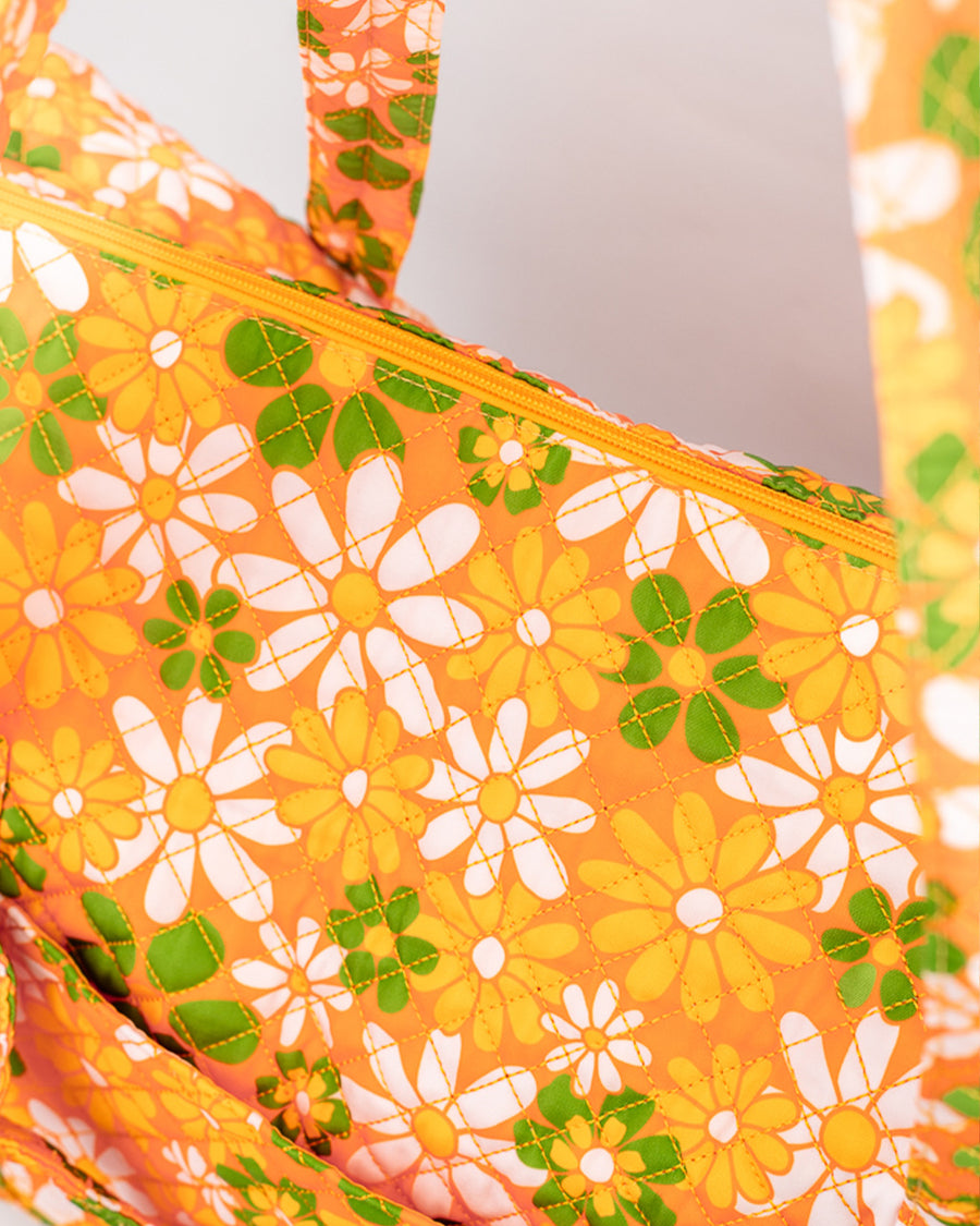 top zipper view of orange quilted duffel bag with handles and adjustable strap and has an all over yellow, white, and green retro floral print