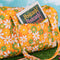 orange quilted duffel bag with handles and adjustable strap and has an all over yellow, white, and green retro floral print with postcard book inside front pocket