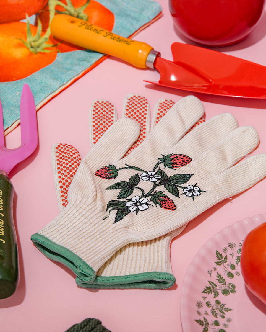 cream gardening gloves with white flower and strawberry print and green trim on a pink table