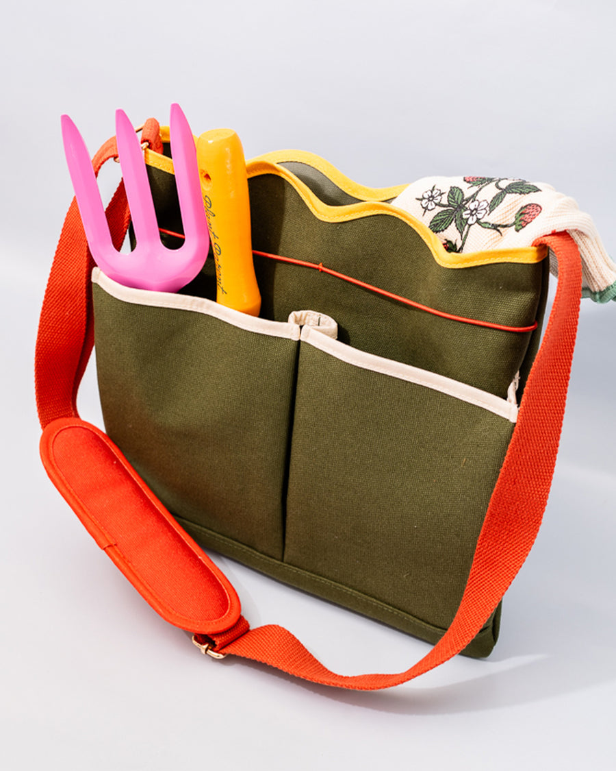 side view of army green canvas gardening tool bag with red strap and yellow scalloped top edge and tools inside