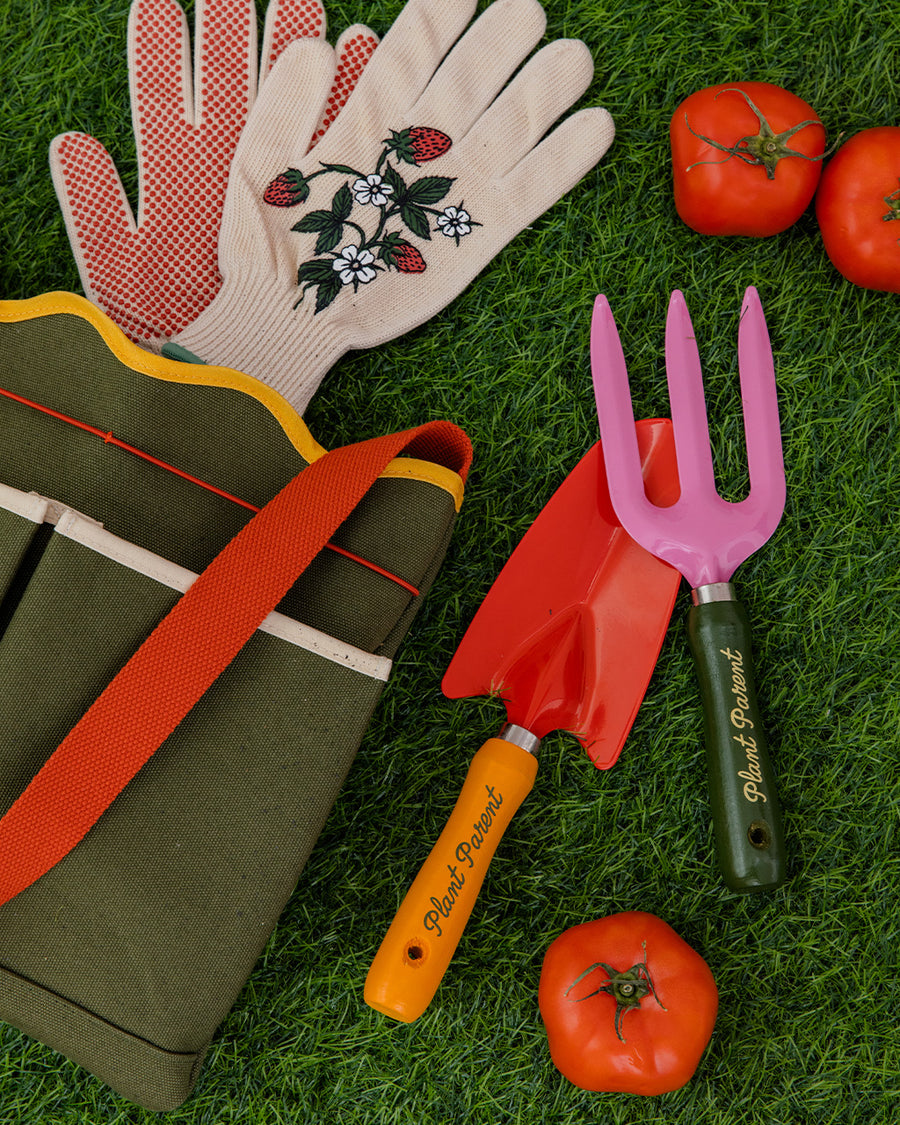 army green canvas gardening tool bag with red strap and yellow scalloped top edge surrounded by gardening items