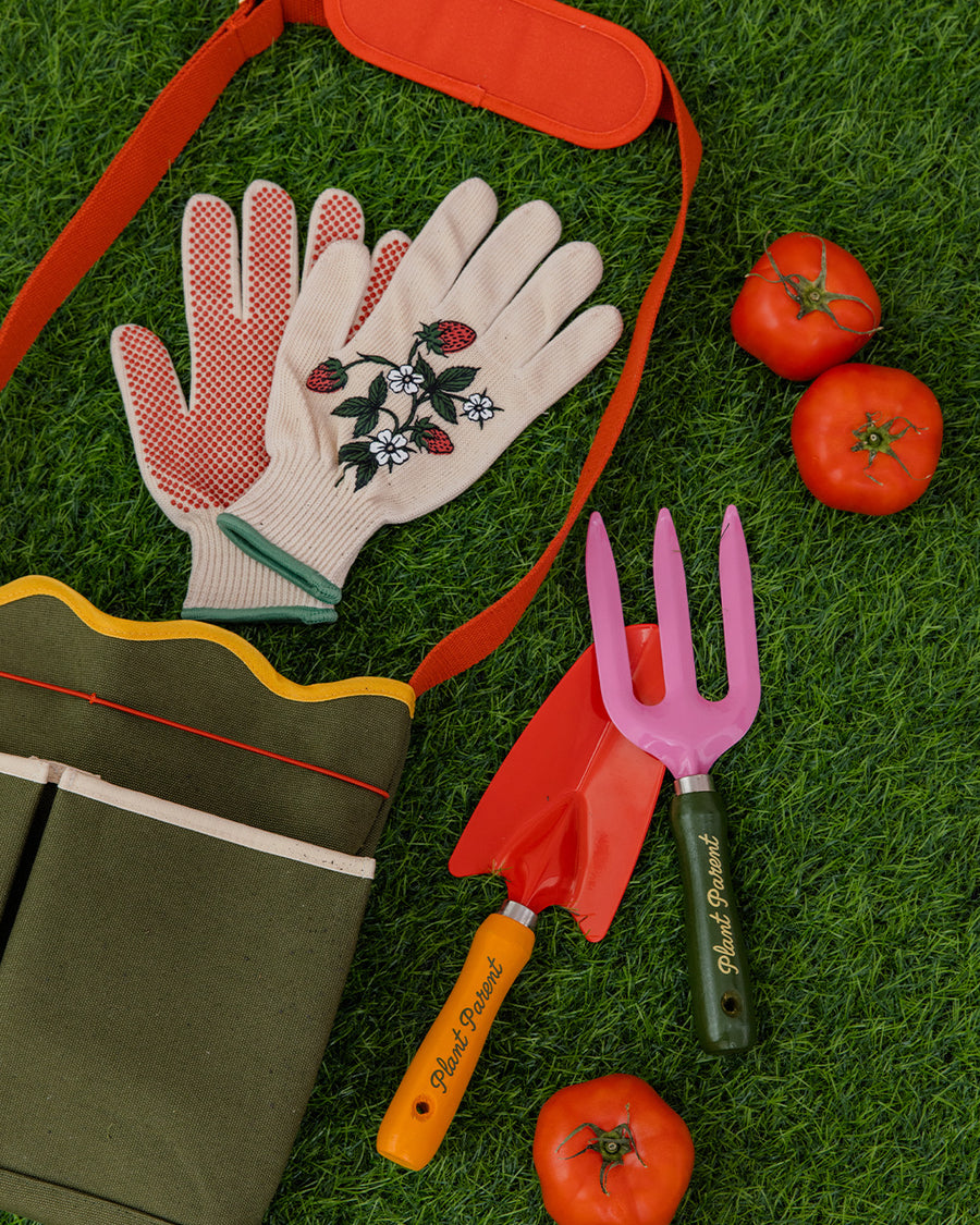 army green canvas gardening tool bag with red strap and yellow scalloped top edge surrounded by gardening items