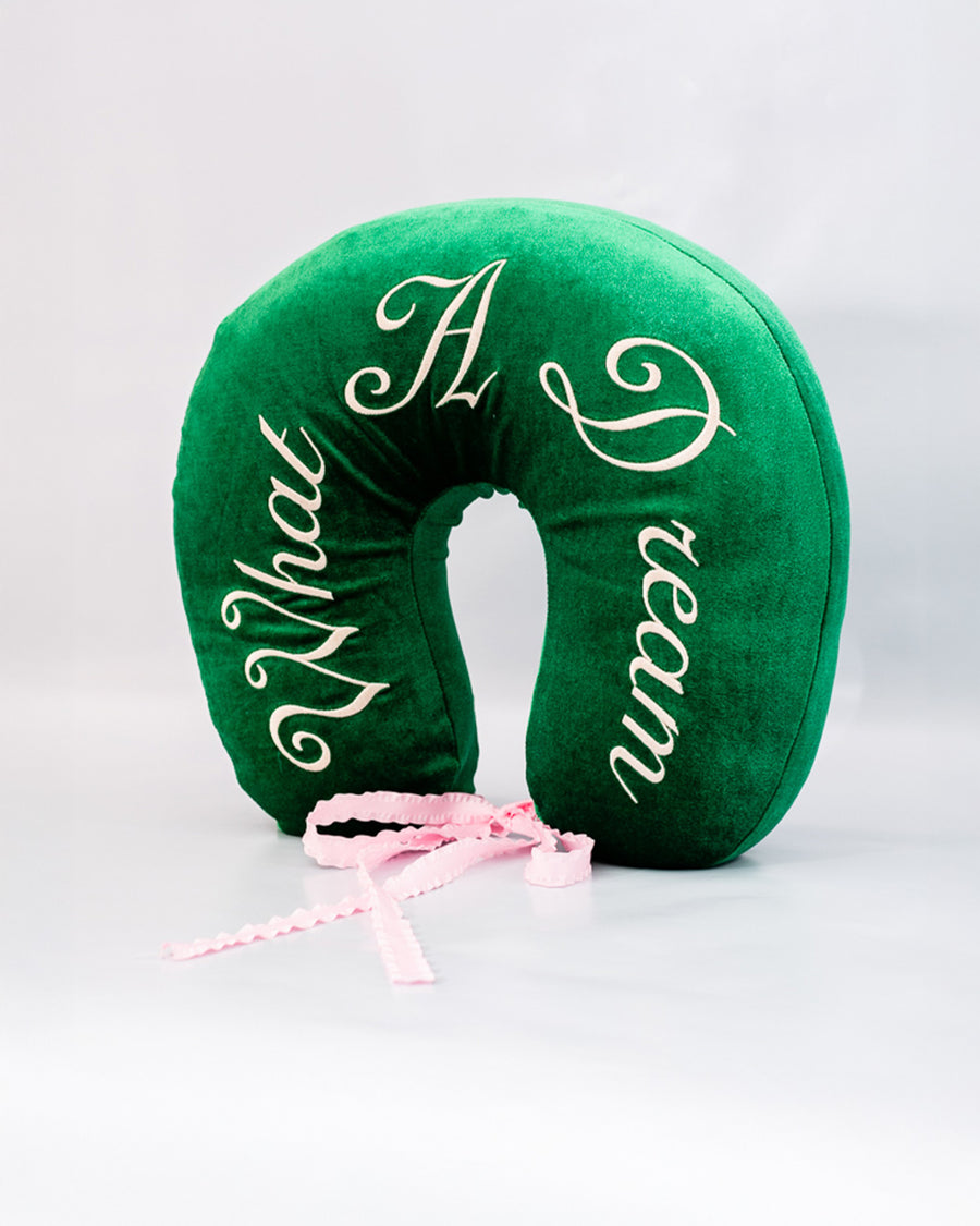 side view of green velvet travel pillow with white 'what a dream' with pink bow