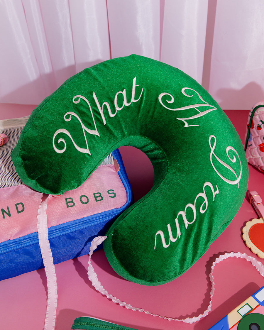 green velvet travel pillow with white 'what a dream' with pink bow on a pink ground