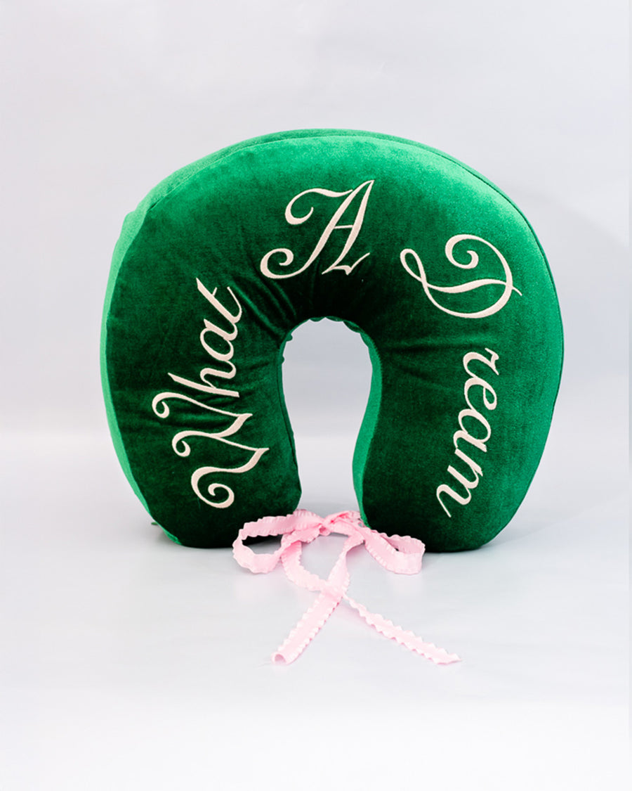 front view of green velvet travel pillow with white 'what a dream' with pink bow