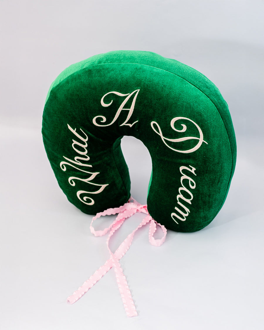 top view of green velvet travel pillow with white 'what a dream' with pink bow