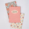 stacked set of 3 pocket notebooks: red vertical stripes with cream circle that says 'growing imperfectly', blue and cream diamond with fruit print, and light blue strawberry and tomato print