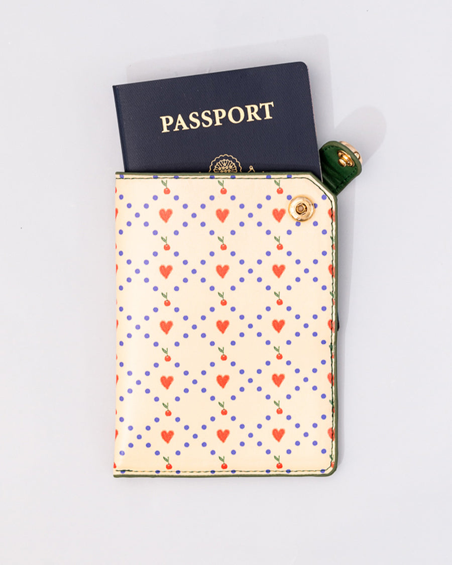 cream passport holder with blue diamond design with hearts and cherries and green side snap closure with a passport sticking out