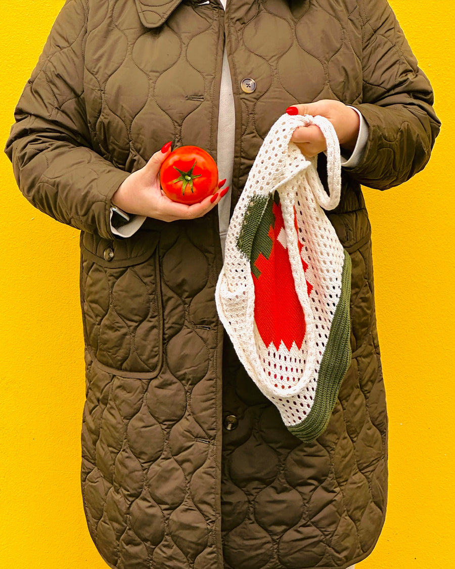 model holding cream open knit market bag with red tomato in the middle and green trim and tomato in the other hand