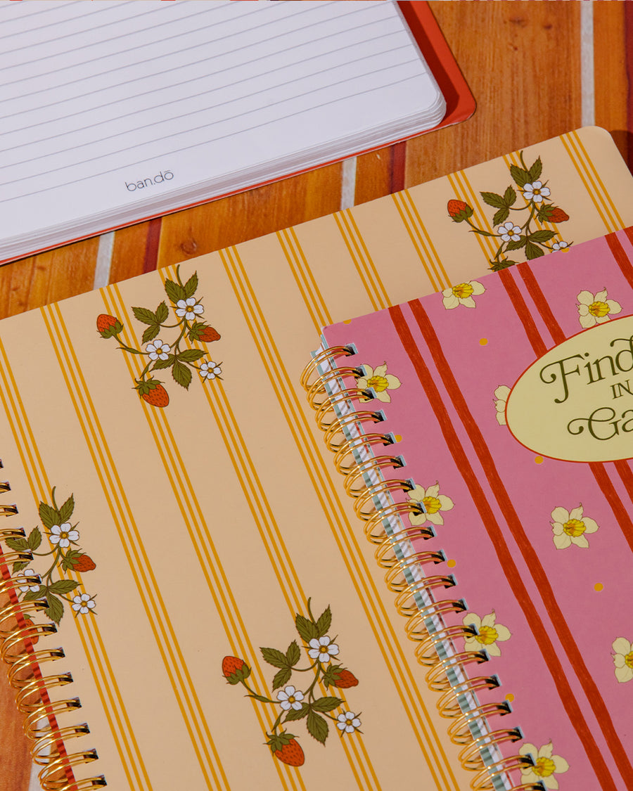 pale yellow large notebook with white floral and strawberry print and dark yellow vertical stripes on a table