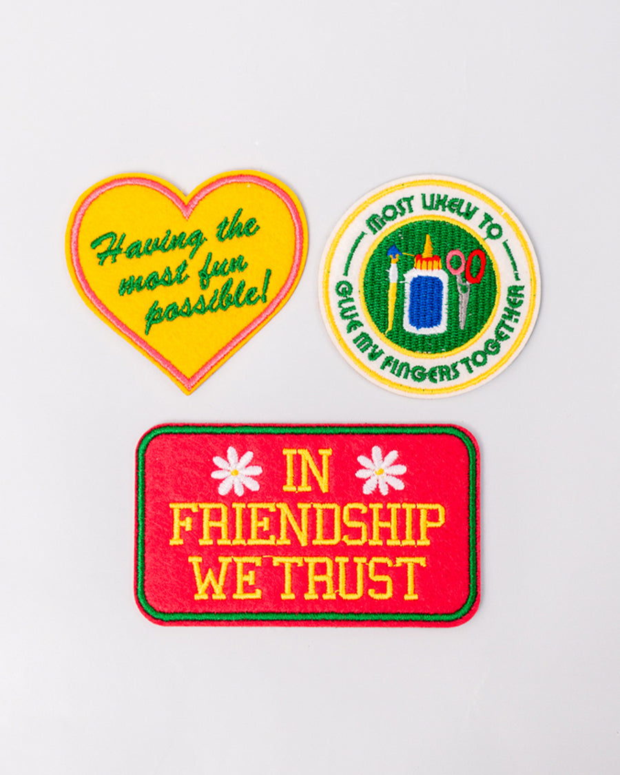 set of 3 embroidered patch stickers: yellow heart with green 'having the most fun possible' across the front, white round 'most likely to glue my fingers together' and red rectangular 'in friendship we trust'