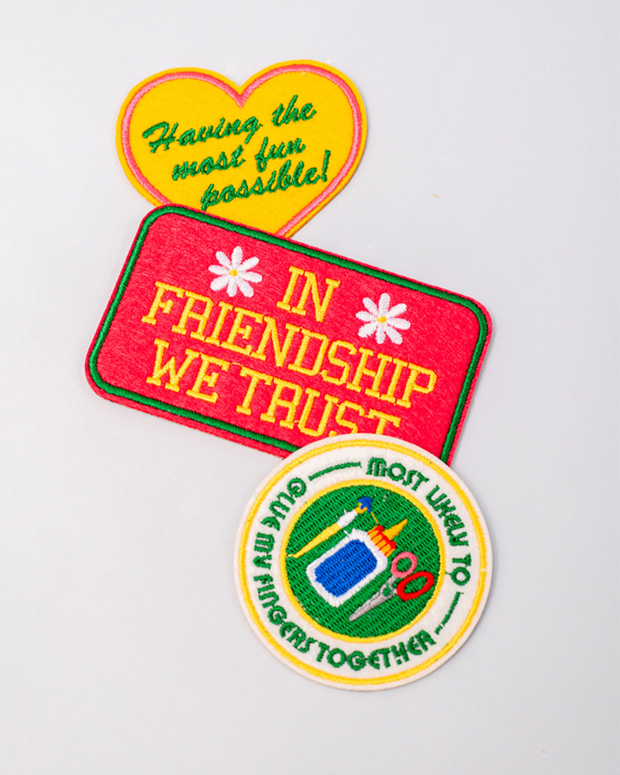 staggered set of 3 embroidered patch stickers: yellow heart with green 'having the most fun possible' across the front, white round 'most likely to glue my fingers together' and red rectangular 'in friendship we trust'