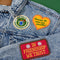 set of 3 embroidered patch stickers: yellow heart with green 'having the most fun possible' across the front, white round 'most likely to glue my fingers together' and red rectangular 'in friendship we trust' on a jean jacket