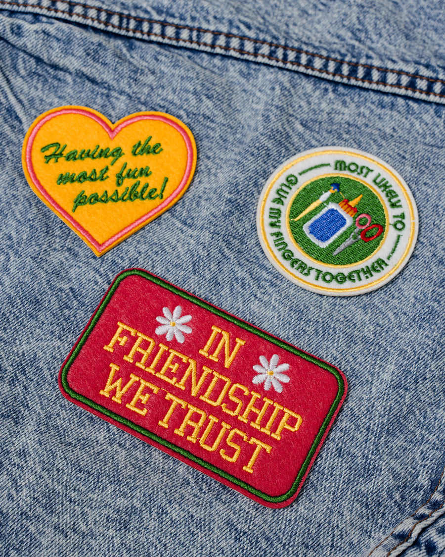 set of 3 embroidered patch stickers: yellow heart with green 'having the most fun possible' across the front, white round 'most likely to glue my fingers together' and red rectangular 'in friendship we trust' on a jean jacket