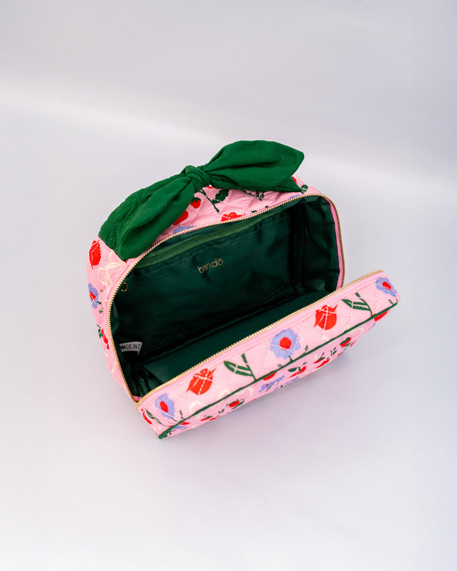 green interior of pink quilted toiletry bag with green bow handle and all over periwinkle flower, cherries, bow and lip print