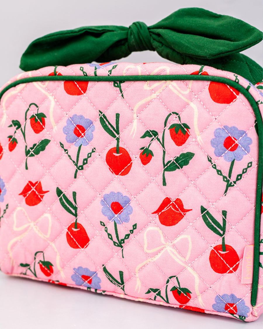 up close of pink quilted toiletry bag with green bow handle and all over periwinkle flower, cherries, bow and lip print