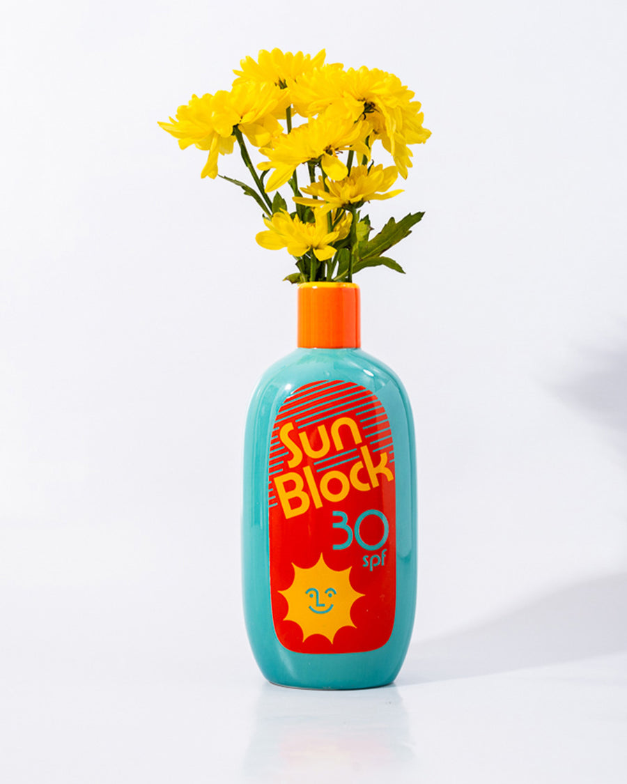 teal ceramic vase with red and yellow 'sunblock 30 SPF' label and yellow flowers inside