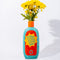 'take a walk on the sunny side' back view of teal ceramic vase with red and yellow 'sunblock 30 SPF' label and yellow flowers inside