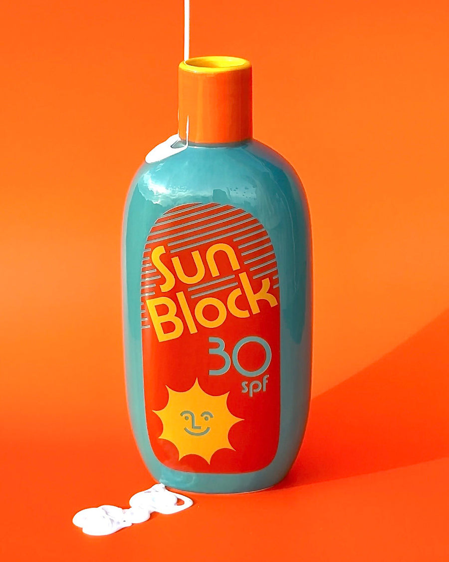  teal ceramic vase with red and yellow 'sunblock 30 SPF' label with sunscreen drizzled on it