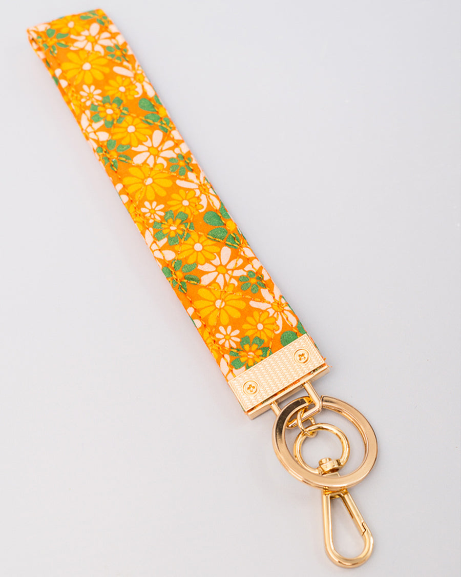 up close of orange wristlet lanyard with white, yellow and green retro floral print and gold hardware