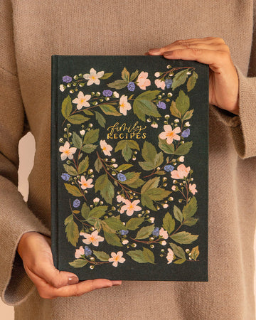 model holding black recipe book with dainty light pink and purple flowers and gold foil 'family recipes' across the front