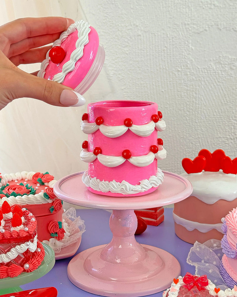 model pulling lid off of hot pink 'tiered' birthday cake jar with white frosting and cherry decorations