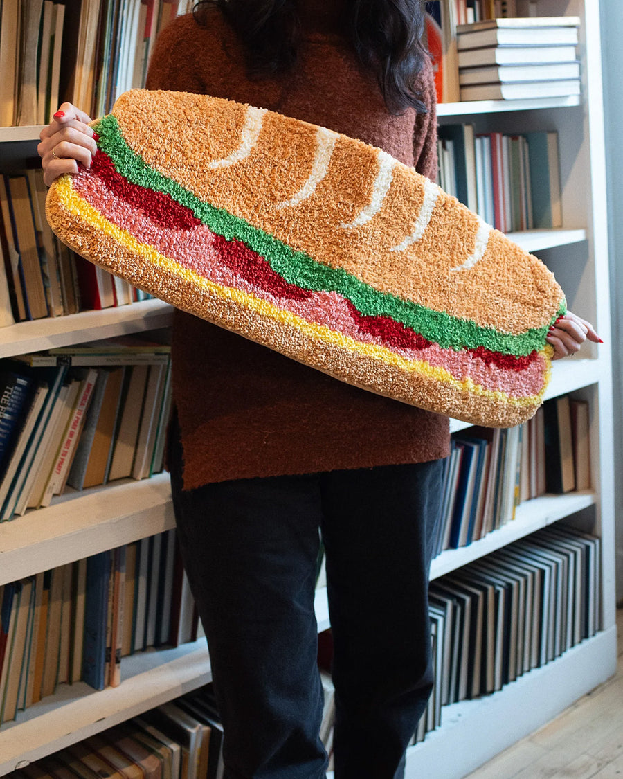 model holding long hoagie shaped throw rug with lettuce, cheese and 'deli meat' center