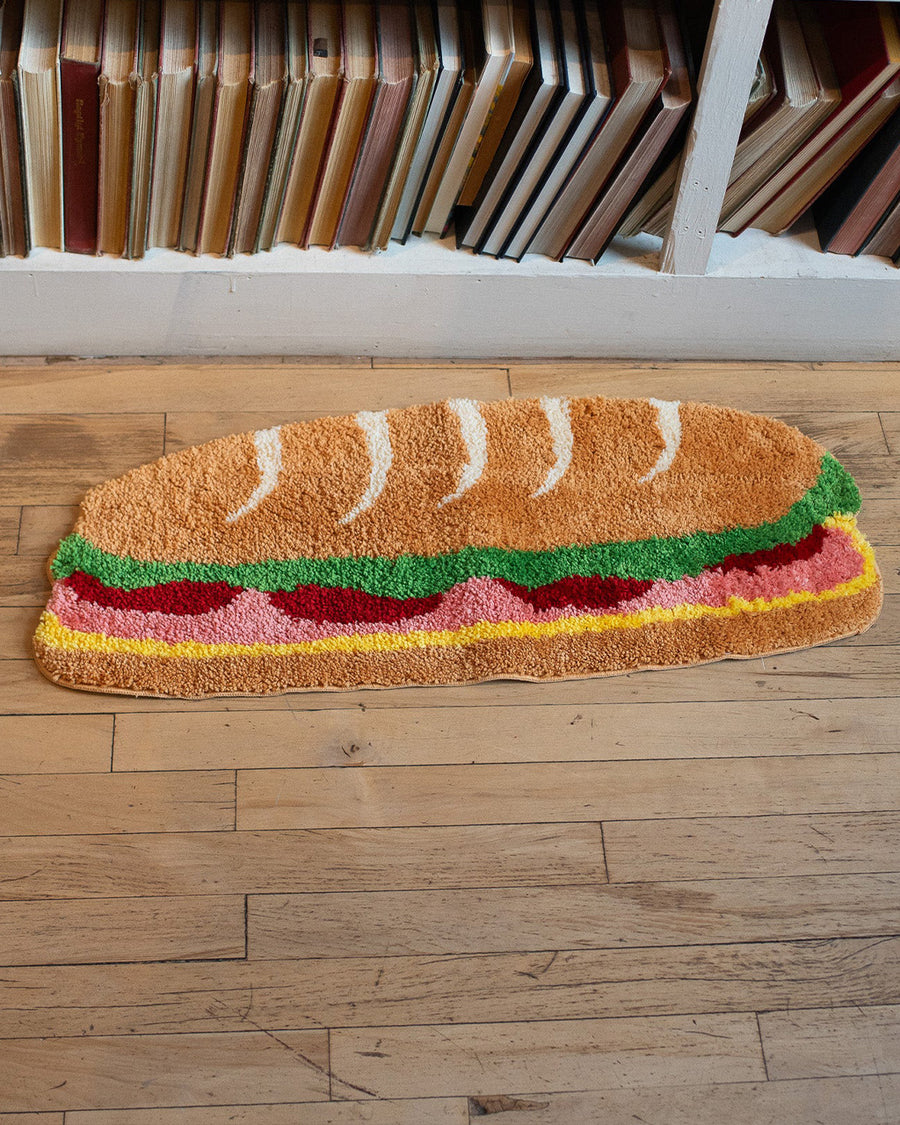 long hoagie shaped throw rug with lettuce, cheese and 'deli meat' center on a floor