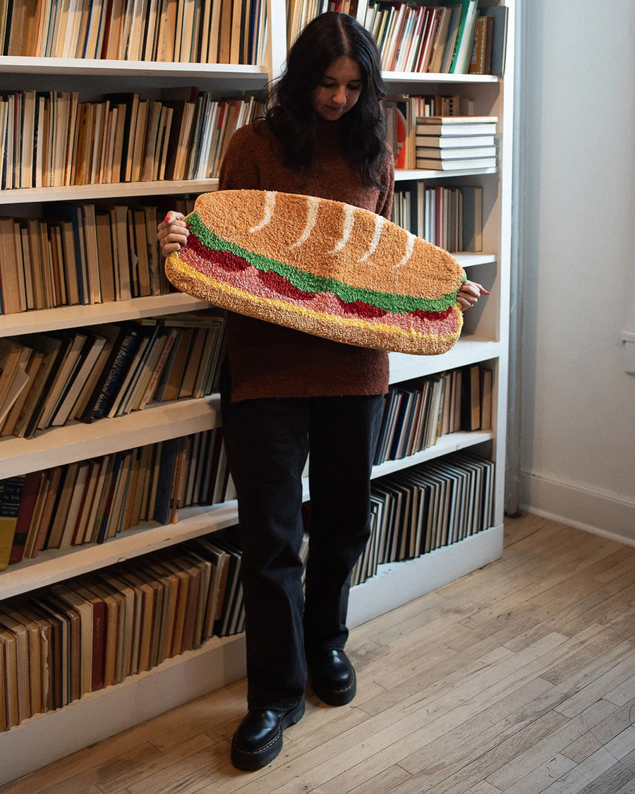 model holding long hoagie shaped throw rug with lettuce, cheese and 'deli meat' center