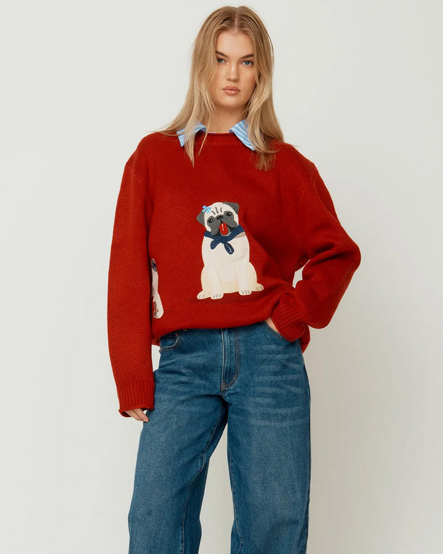 front view of model wearing red oversized crew sweater with pug wearing a blue bow and bandana on the front