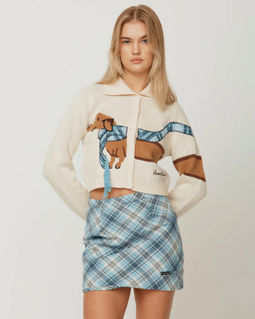 model wearing cream cropped cardigan with a dog wearing a blue plaid scarf across the front and back