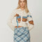 model wearing cream cropped cardigan with a dog wearing a blue plaid scarf across the front and back