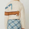 back view of model wearing cream cropped cardigan with a dog wearing a blue plaid scarf across the front and back